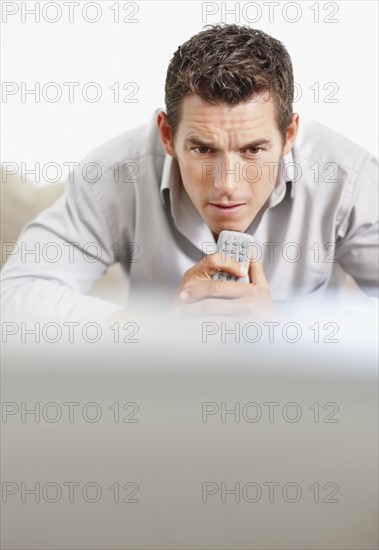 Tense man holding remote control in front of television. Photo : Momentimages