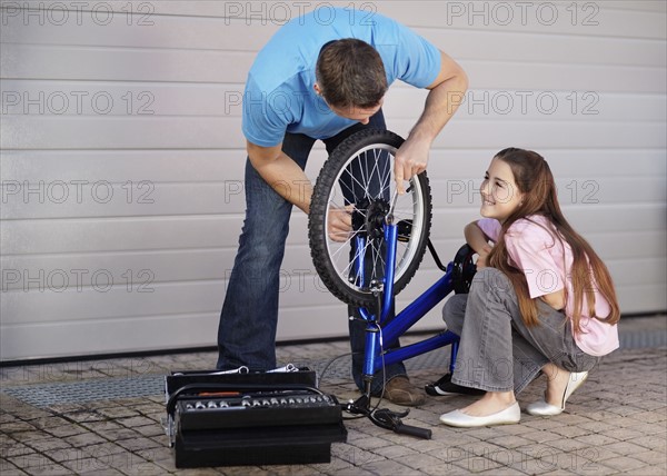 Father with daughter (10-11) fixing bike. Photo : Momentimages