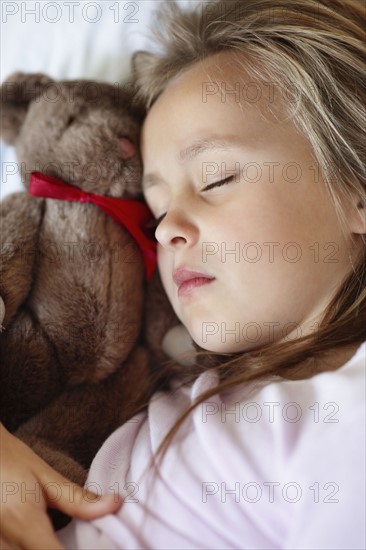 Sad girl (10-11) sleeping in bed with teddybear. Photo : Momentimages