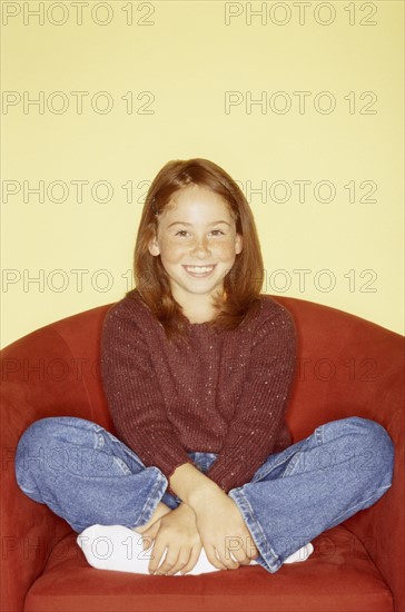 Cute young girl sitting in red chair. Photo : Fisher Litwin