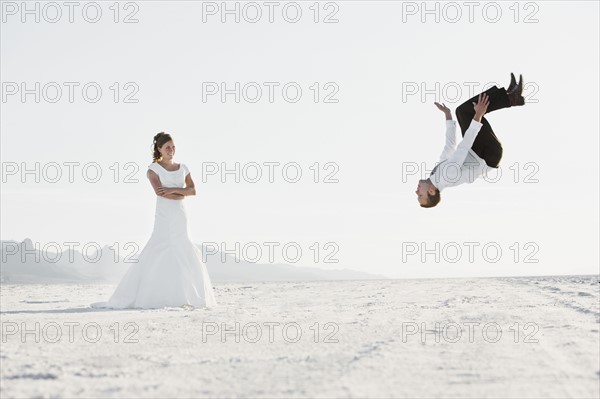 Bride watching groom performing backflip in desert. Photo : FBP