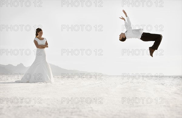 Bride watching groom performing backflip in desert. Photo : FBP
