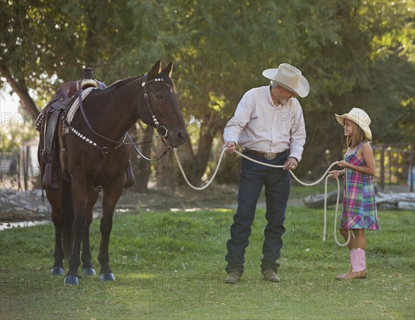 Senior man with granddaughter (8-9) training horse in ranch. Photo : Mike Kemp