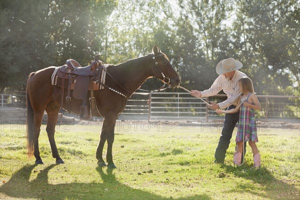 Senior man with granddaughter (8-9) training horse in ranch. Photo : Mike Kemp