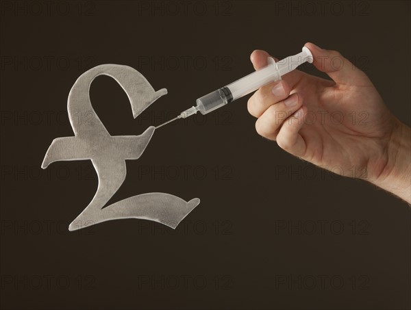 Hand holding syringe on "Pound" sign. Photo : Mike Kemp