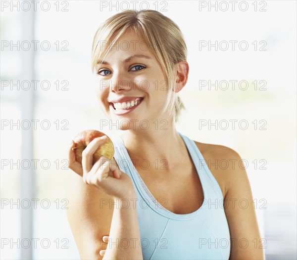 Portrait of young blonde woman holding apple. Photo : Momentimages