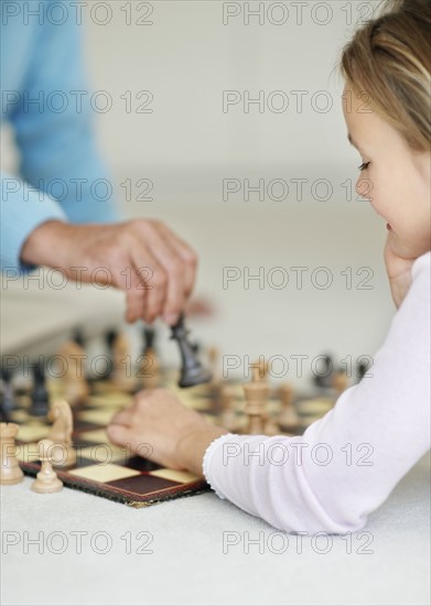 Granddaughter (10-11) playing chess with grandfather. Photo : Momentimages