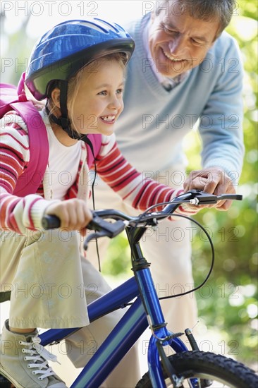 Grandfather helping granddaughter (10-11) riding bike. Photo : Momentimages