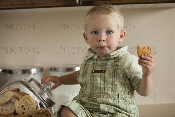 Portrait of baby boy (12-17 months) holding cookie in kitchen. Photo : Mike Kemp