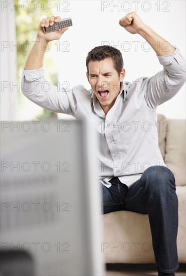 Man cheering in front of television. Photo : Momentimages