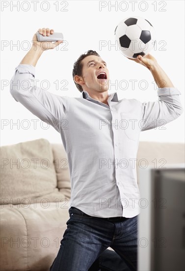 Mid adult man watching football match on television. Photo : Momentimages