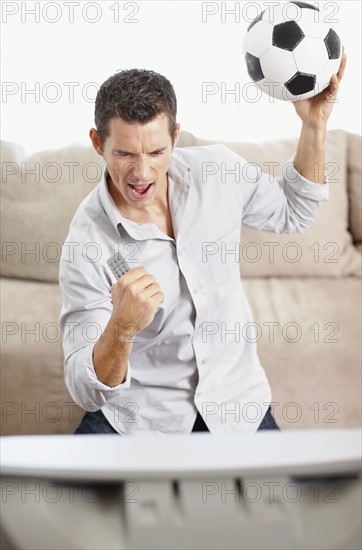 Mid adult man watching football match on television. Photo : Momentimages