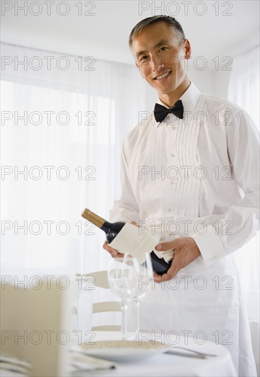 Smiling waiter holding champagne bottle and looking at camera. Photo : Jamie Grill