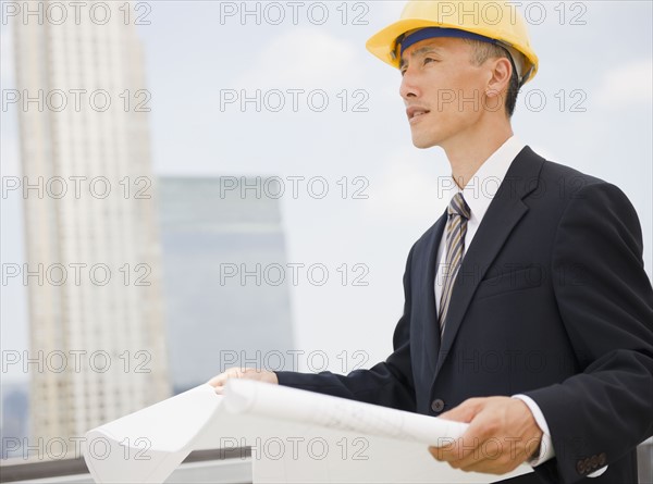 Engineer holding plans, wearing protective helmet and looking away. Photo : Jamie Grill