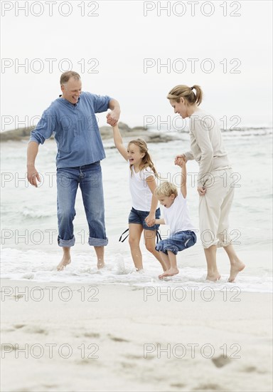 Girl (10-11) and boy (4-5) playing on beach with parents. Photo : Momentimages