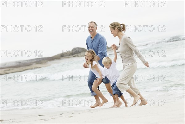 Girl (10-11) and boy (4-5) playing on beach with parents. Photo : Momentimages