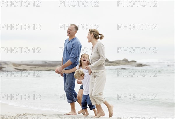 Girl (10-11) and boy (4-5) playing on beach with parents. Photo : Momentimages