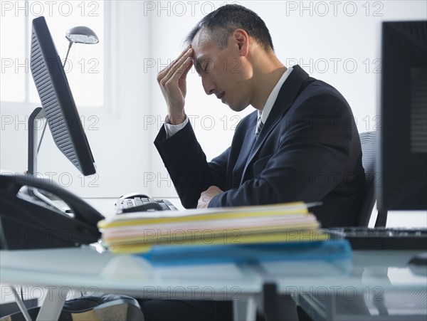Businessman with headache sitting in office. Photo : Jamie Grill