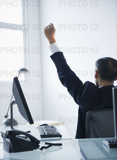 Businessman with raised fist sitting in office. Photo : Jamie Grill