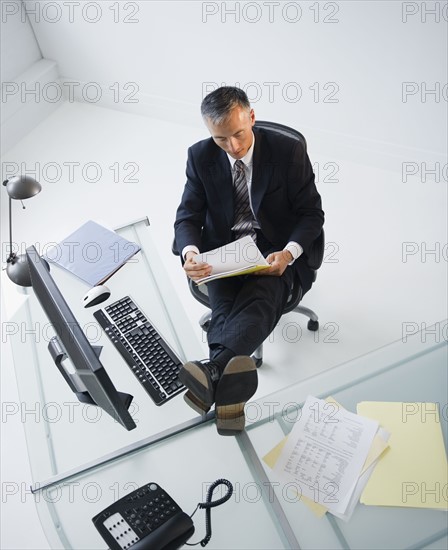 Businessman reading documents in office with feet on desk. Photo : Jamie Grill