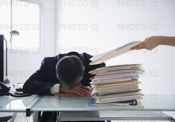 businessman with head on desk and pile of documents in front of him. Photo : Jamie Grill