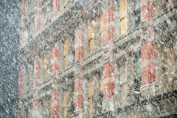 Snow falling in front of apartment building.