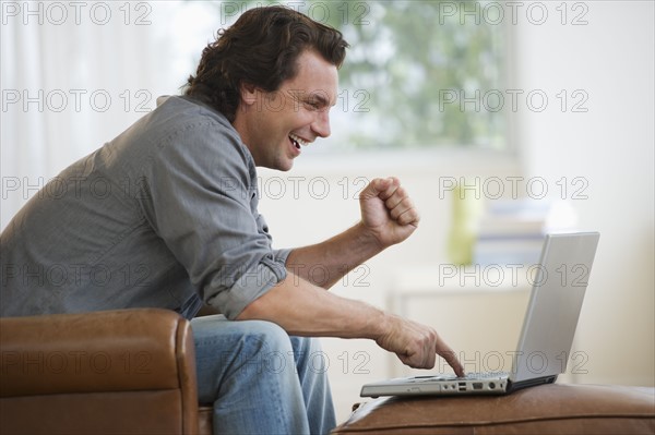 Man on armchair using laptop and laughing.