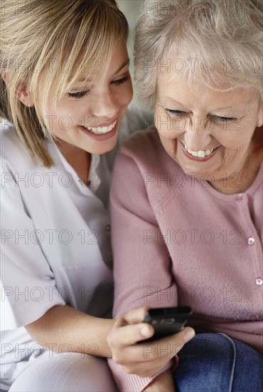 Daughter and mother checking mobile phone and smiling. Photo : Momentimages