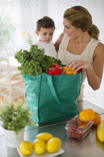 Mother and daughter (12-18 months) unpacking shopping bag.