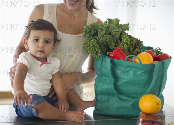 Mother and daughter (12-18 months) unpacking shopping bag.