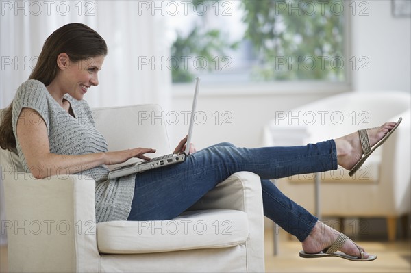 Woman on armchair using laptop and laughing.