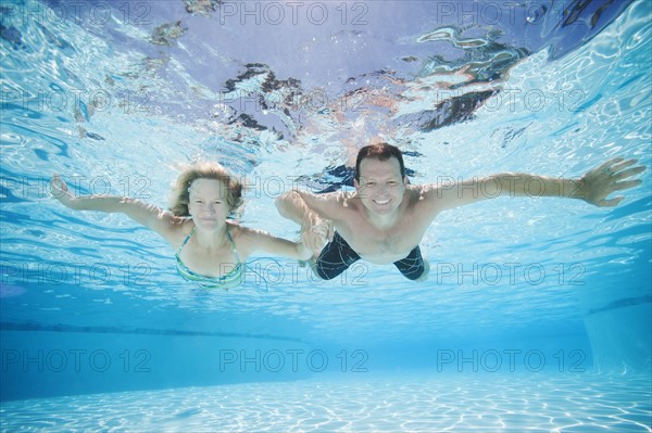 Mid adult couple swimming underwater.