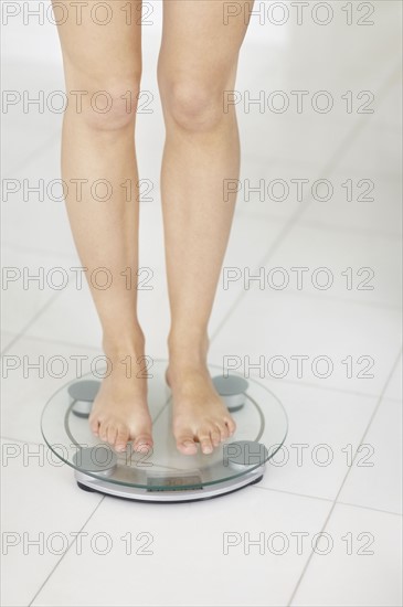 Young woman standing on bathroom scale. Photo : Momentimages