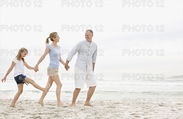 Parents with daughter (10-11) walking on beach. Photo : Momentimages