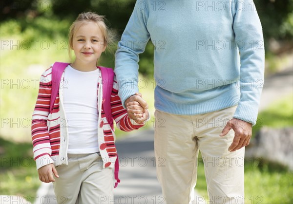 Granddaughter (10-11) and grandfather walking through parkholding hands. Photo : Momentimages