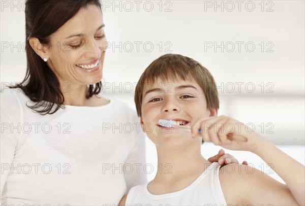 Mother embracing son (12-13)  while he is brushing teeth. Photo : Momentimages