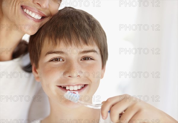 Mother embracing son (12-13) while he is brushing teeth. Photo : Momentimages