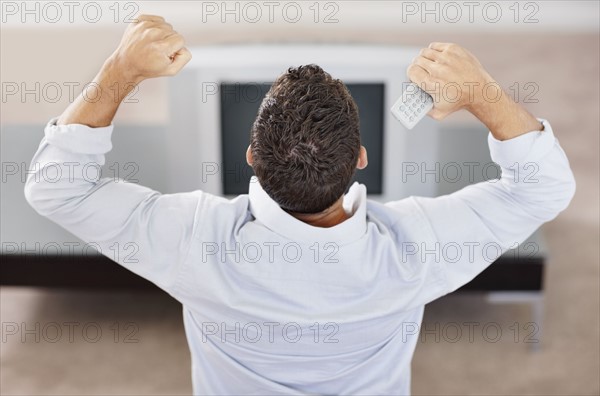 Man cheering in front of television. Photo : Momentimages