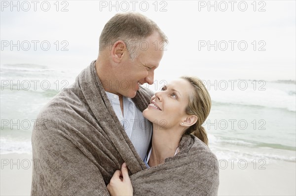 Embraced couple covered by blanket looking each other. Photo : Momentimages