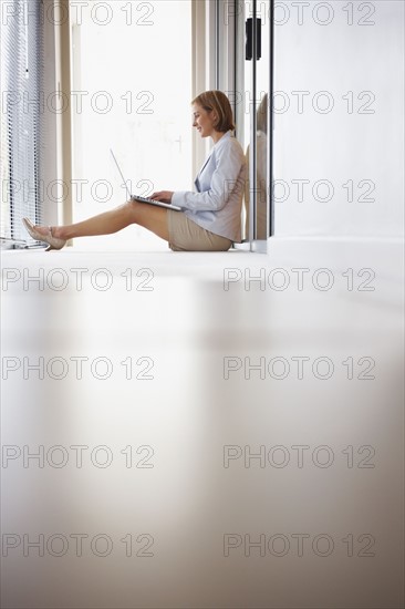 Businesswoman sitting in corridor with laptop. Photo : Momentimages