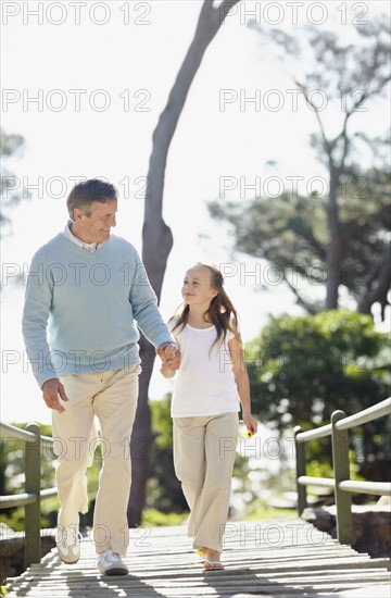 Granddaughter (10-11) and grandfather walking on bridgeholding hands. Photo : Momentimages