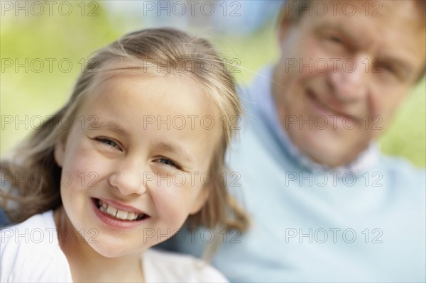 Portrait of happy girl (10-11)grandfather in background. Photo : Momentimages