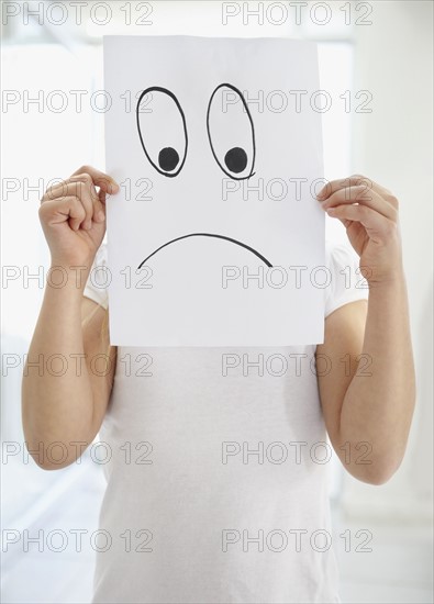 Girl (10-11) girl holding 'sad face' in front of herself. Photo : Momentimages