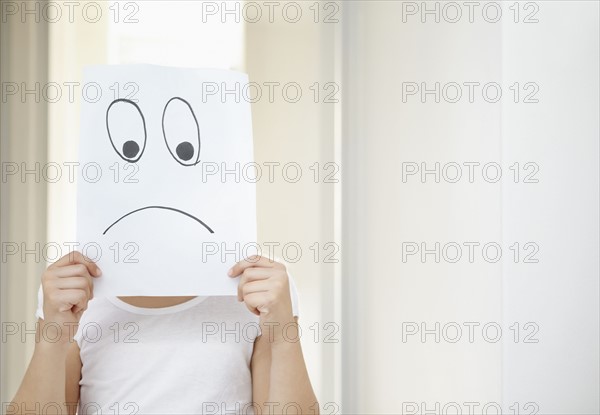 Girl (10-11) girl holding 'sad face' in front of herself. Photo : Momentimages