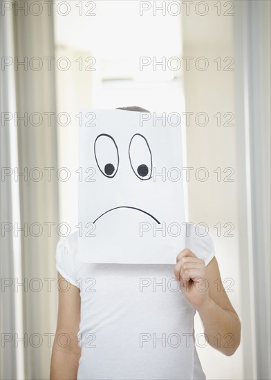Girl (10-11) girl holding 'sad face' in front of herself. Photo : Momentimages