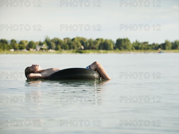 Boy (12-13) floating on rubber ring on lake.