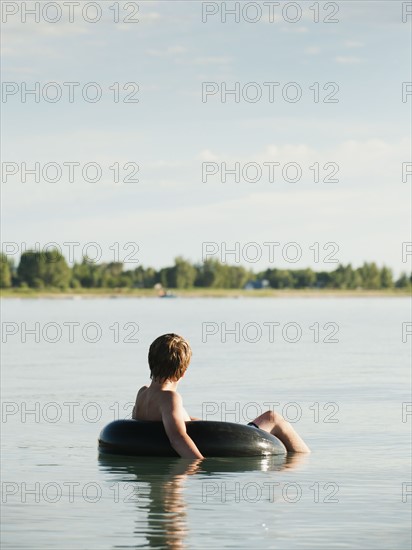 Boy (12-13) floating on rubber ring on lake.