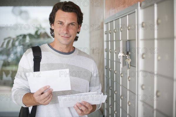 Man standing next to mailboxes and holding letters.