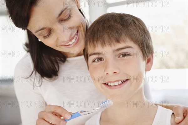 Mother embracing son (12-13) while he is brushing teeth. Photo : Momentimages