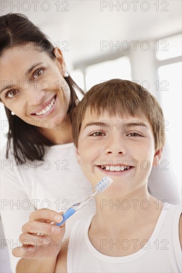 Mother embracing son (12-13) while he is brushing teeth. Photo : Momentimages